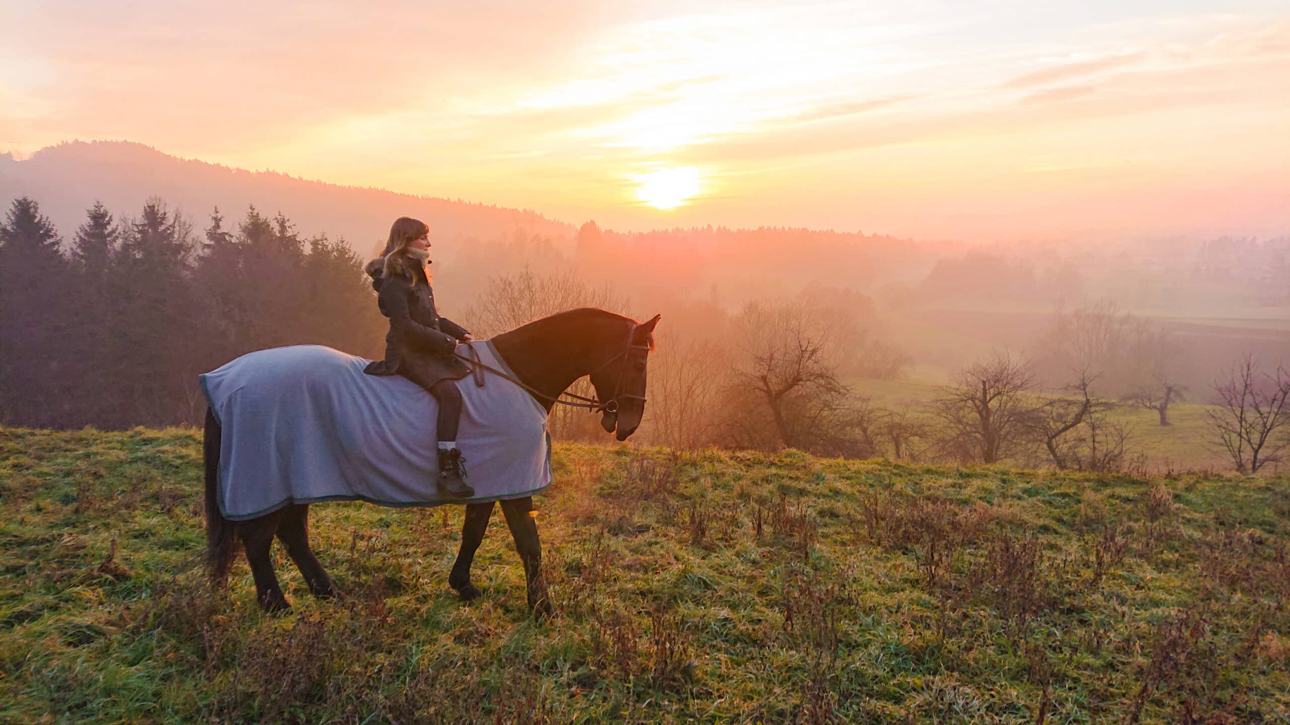 The Trainers Loft horse blanket guide, Young female riding a blanket covered stallion around the countryside in winter.