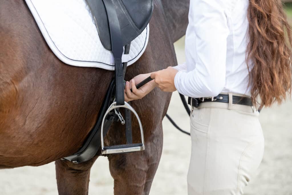 The Trainer's Loft Used Tack, Woman tightens the cinch on a saddle.