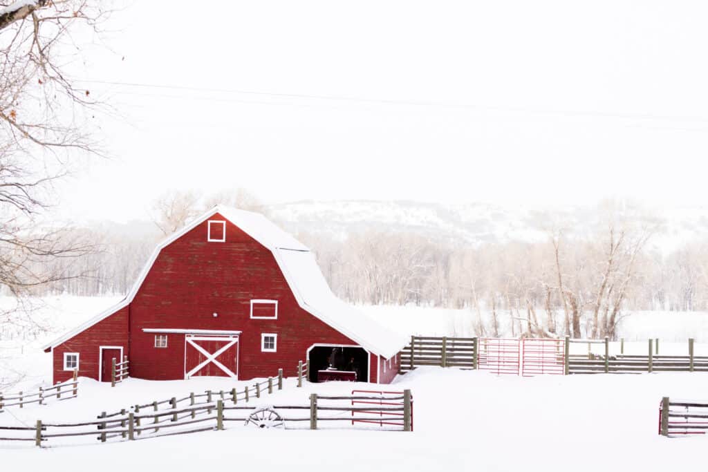 The Trainers Loft Winter Horse Care, red barn in snow on hill