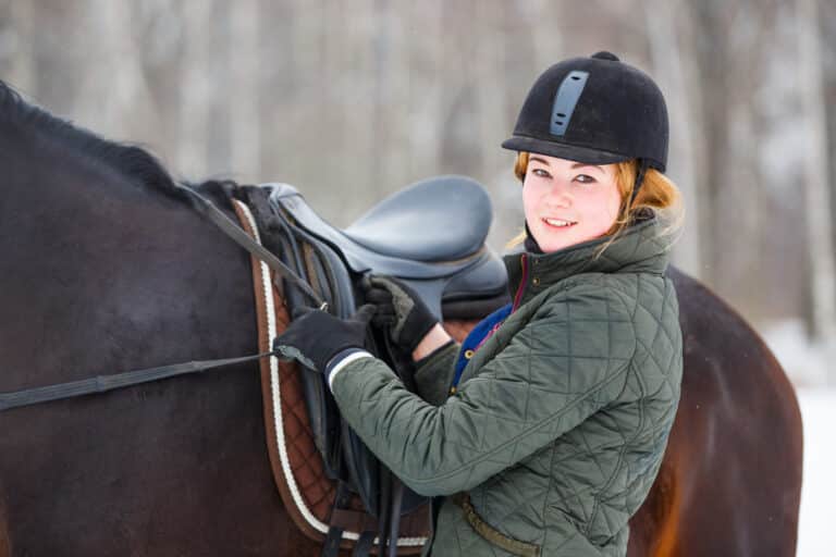 The Trainer's Loft Saddlery, Young woman adjusting stirrups before riding horse