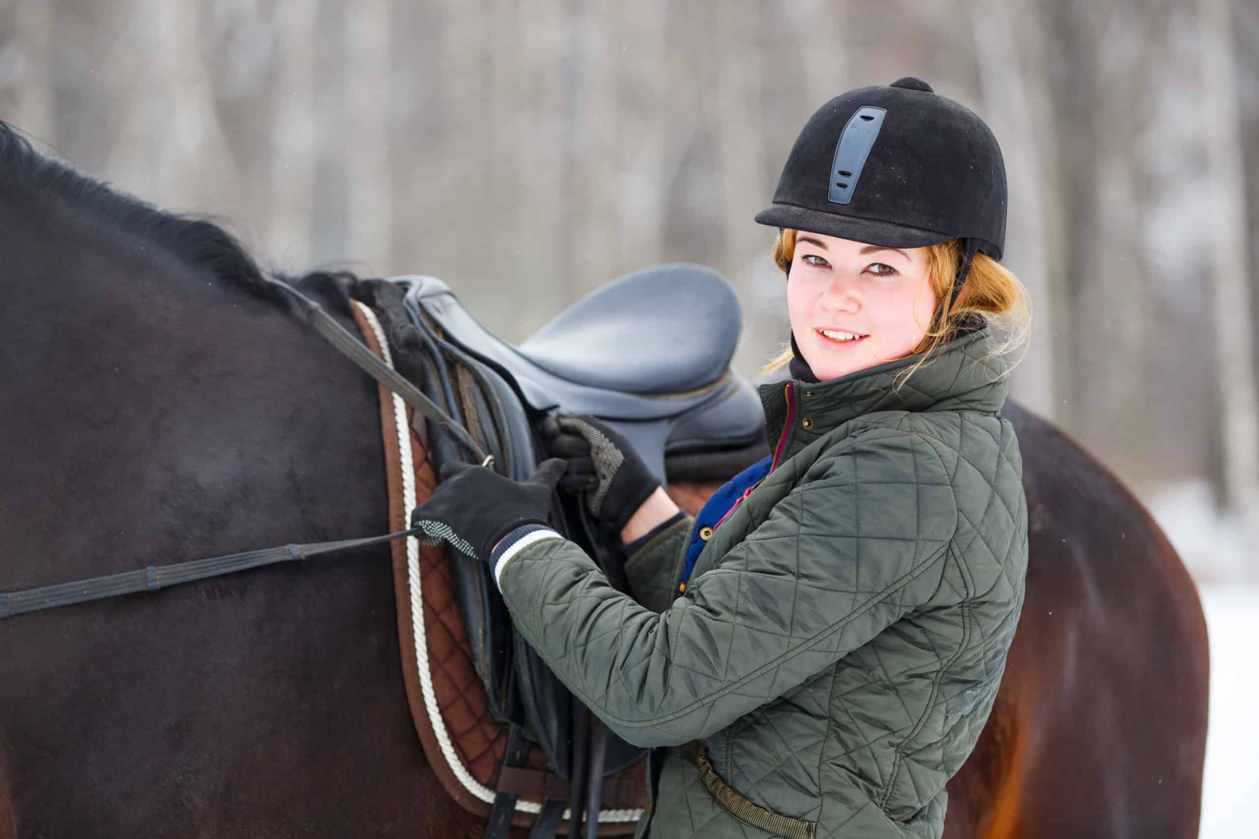The Trainer's Loft Saddlery, Young woman adjusting stirrups before riding horse